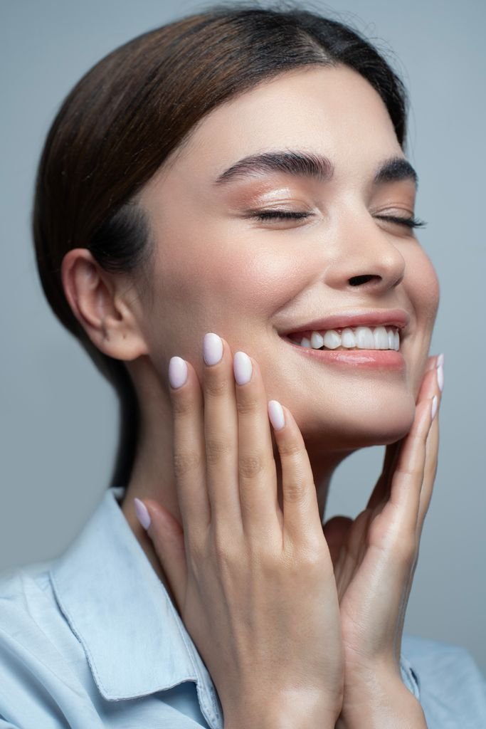 A close-up portrait of a woman smiling with closed eyes, showcasing her radiant skin and beauty.